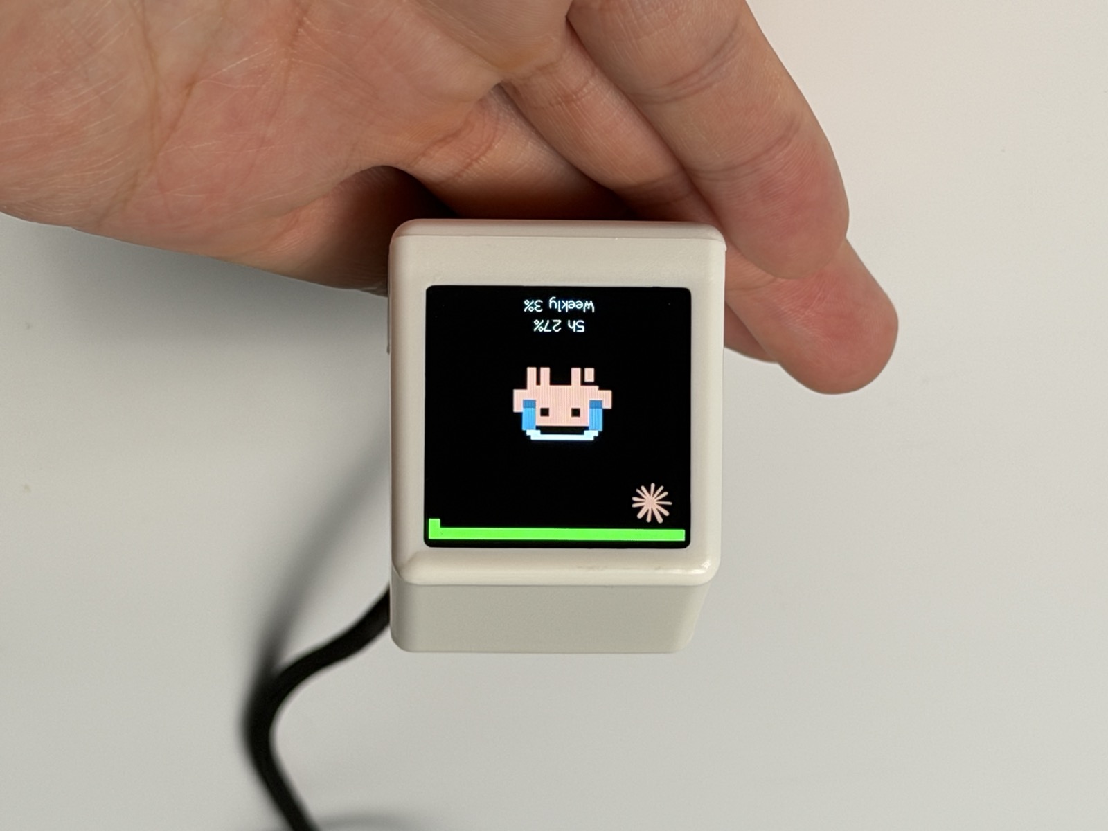 手心里的 AI Mac 小屏幕，屏幕上显示戴耳机的像素桌宠和 5h / 周额度百分比